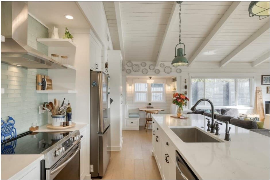 A calm kitchen angle showing the sink, island, open shelves, and morning light