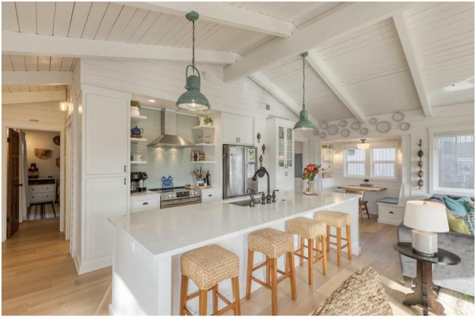 A bright kitchen with white beams, woven stools, and an island at the center