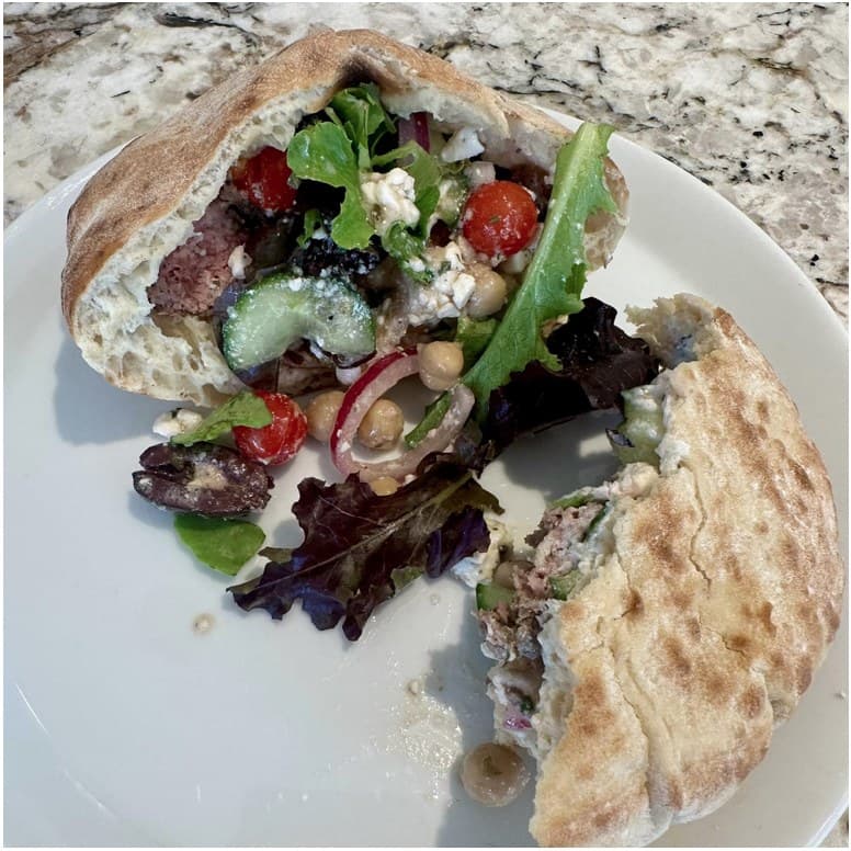 A pita sandwich opened next to a simple salad on a white plate