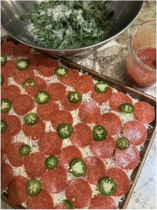 A sheet pan pizza topped with pepperoni, jalapenos, and grated cheese beside salad greens